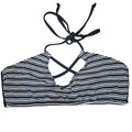 A black and white vertically striped bikini top with black tie straps, laid flat on a gray wood-look floor.